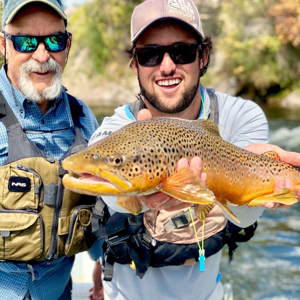 two men showing the fish they caught in a float boat on the river in Aspen