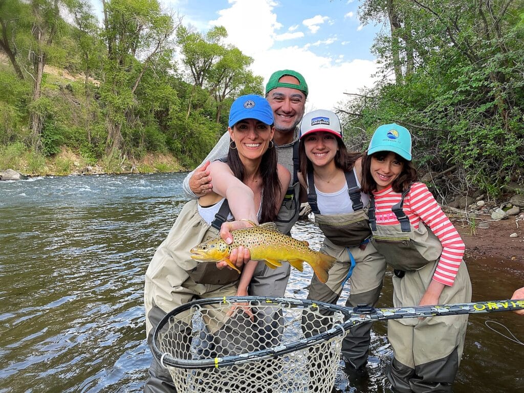 family wade fishing in Colorado showing off a rainbow trout