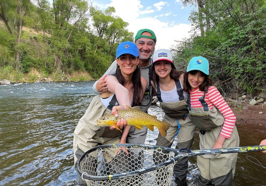 family wade fishing in Colorado showing off a rainbow trout