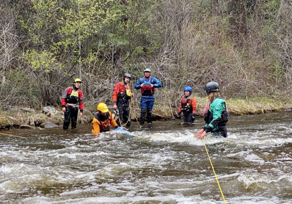 6 men in dry suits are in the Roaring Fork River practicing using a throw rope